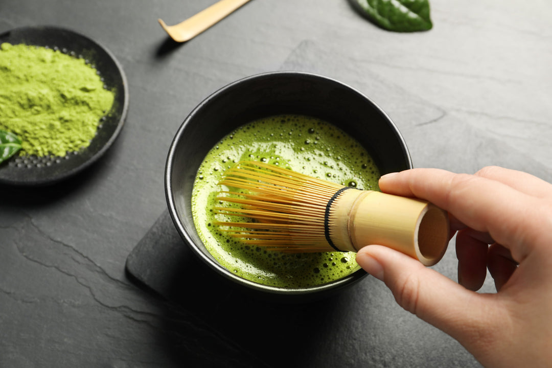 Hand rührt Matcha in einer Schale mit Besen