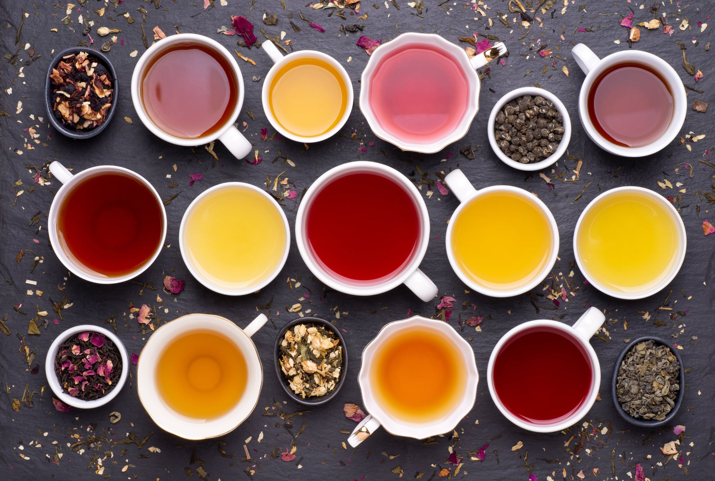 verschiedene Tees aufgebrüht in Teetassen auf einer schwarzen Steinplatte